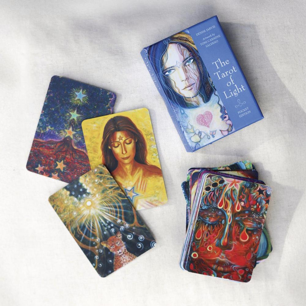 The Tarot of Light oracle card deck and several illustrated cards arranged on a light fabric background. The box shows a blue-toned portrait and the card backs feature colorful abstract and cosmic artwork.