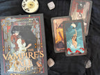 A tarot card deck box labeled 'The Vampire's Star Arc' is displayed on a dark fabric background with several cards fanned out beside it and small stones around it.
