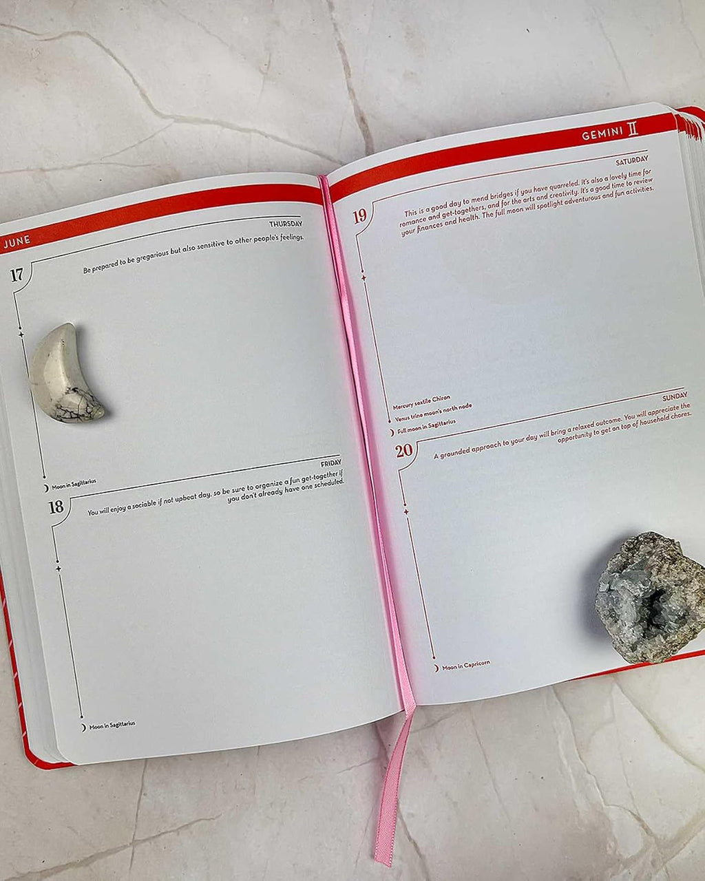 An open book with red and pink edges, showing printed pages with numbered exercises and small inset photos of stones. The book is photographed from above on a light stone or marble surface.