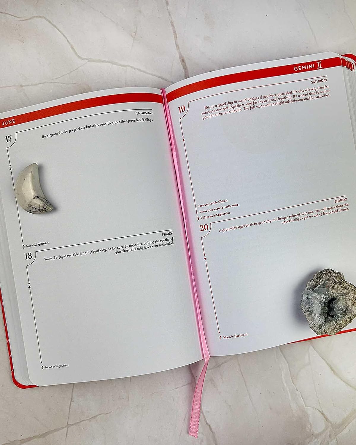 An open book with red and pink edges, showing printed pages with numbered exercises and small inset photos of stones. The book is photographed from above on a light stone or marble surface.