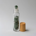 Clear glass roller bottle with green stones and wooden cap on a light gray background