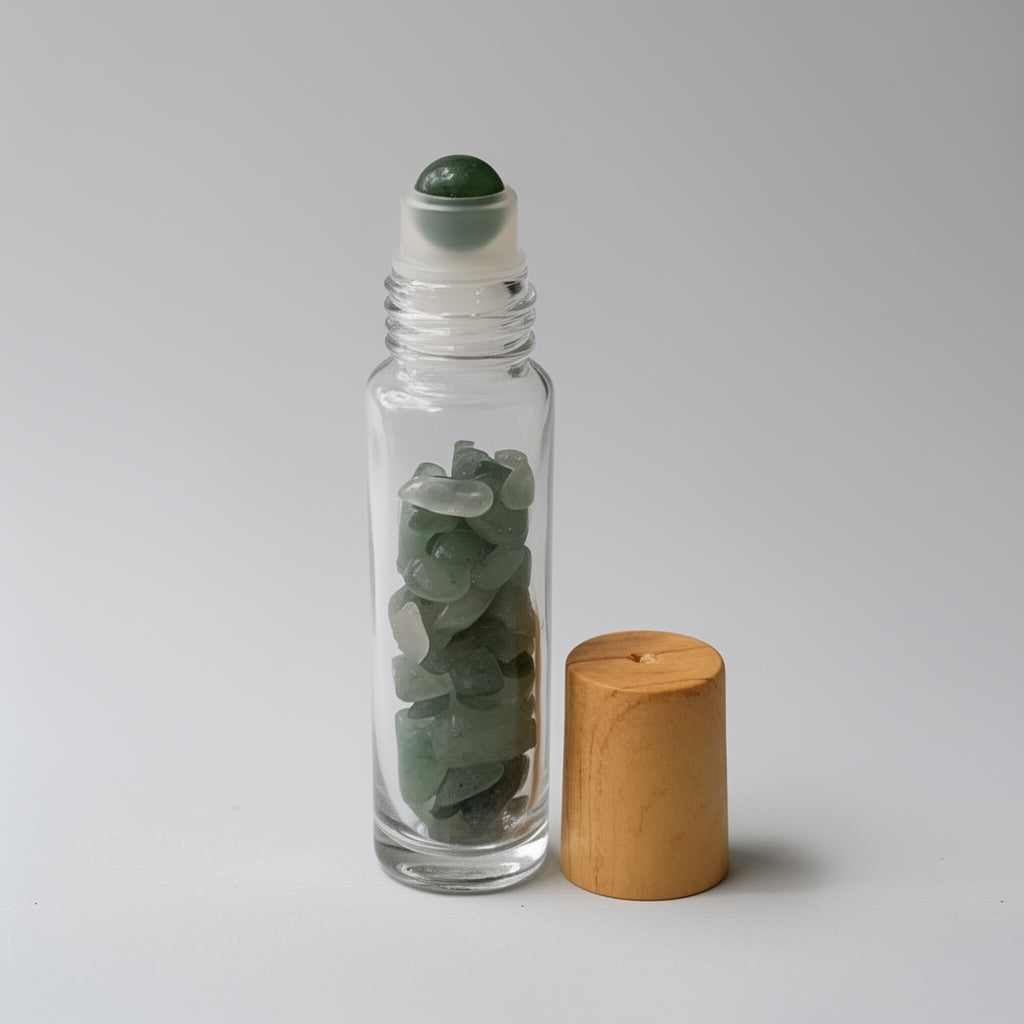 Clear glass roller bottle with green stones and wooden cap on a light gray background