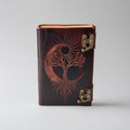 Brown leather notebook with tree of life design and gold latches on a gray background