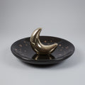 Black dish with a gold crescent moon on a gray background