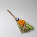 Decorative broom with flowers and a blue eye charm on a light gray background