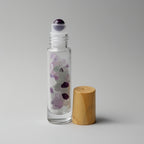 Clear glass roller bottle with wooden cap on a gray background