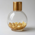 Clear glass bottle with gold cap and gold flakes on a light gray background