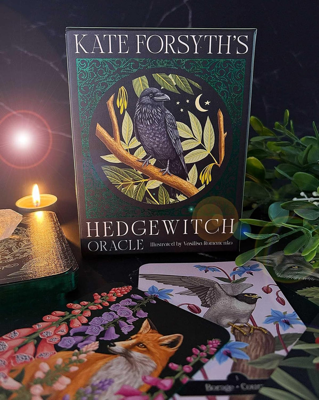 Kate Forsyth’s Hedgewitch Oracle box with raven artwork, beside illustrated fox and bird cards, greenery and a lit candle.