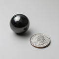 Black sphere next to a U.S. quarter dollar on a light gray background