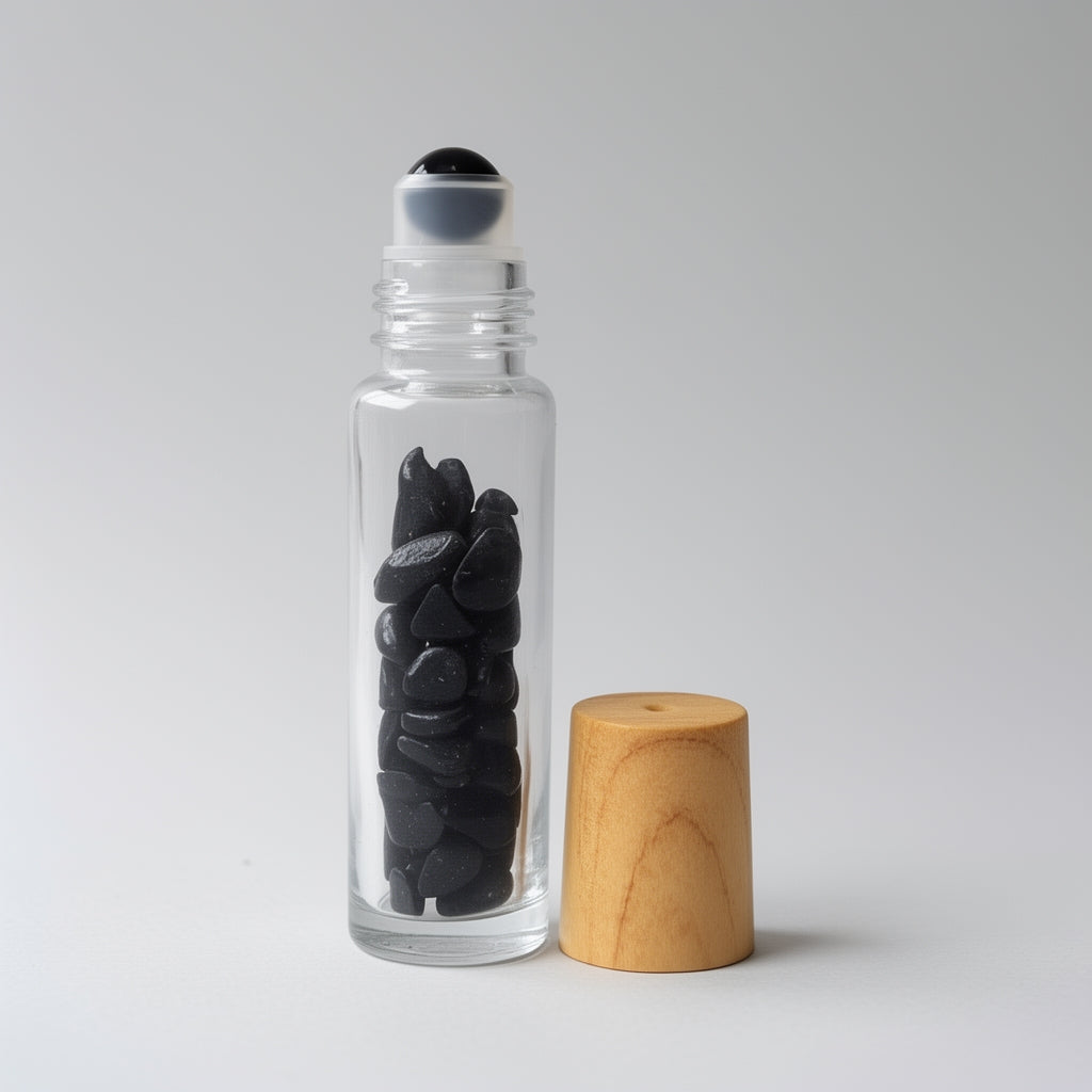 Clear glass roller bottle with black stones and wooden cap on a light gray background