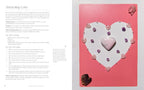 An open book spread showing a guide titled 'Attracting Love' with text on the left page and a pink heart-shaped crystal grid kit on the right page, decorated with pink and purple crystals and a central heart.