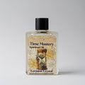 Bottle of 'Time Mastery Spiritual Oil' with hourglass design on label against a gray background